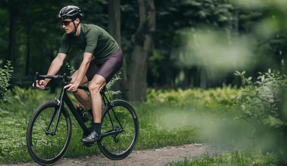 Cyklist i olivengrøn trøje på fart ned ad en skovsti